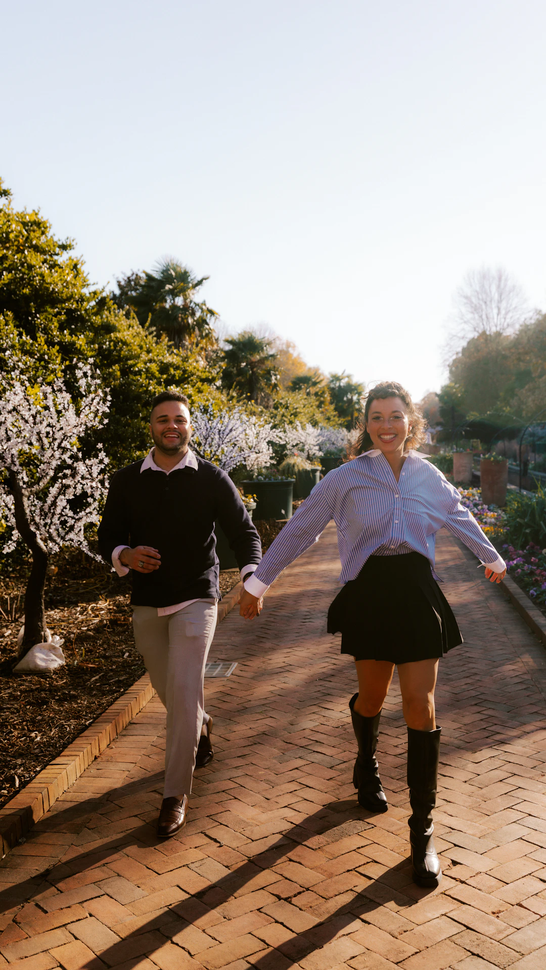 Couple holding hands walking on brick path in park.
