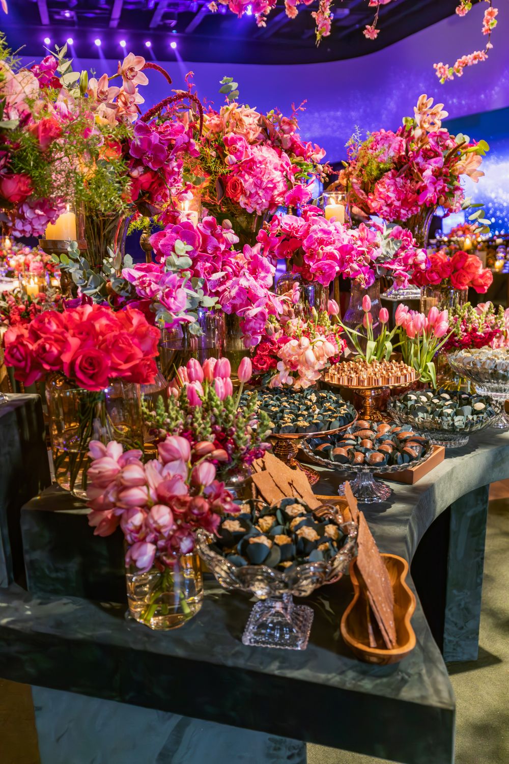 A vibrant display of flowers and desserts at a lavish indoor celebration event.