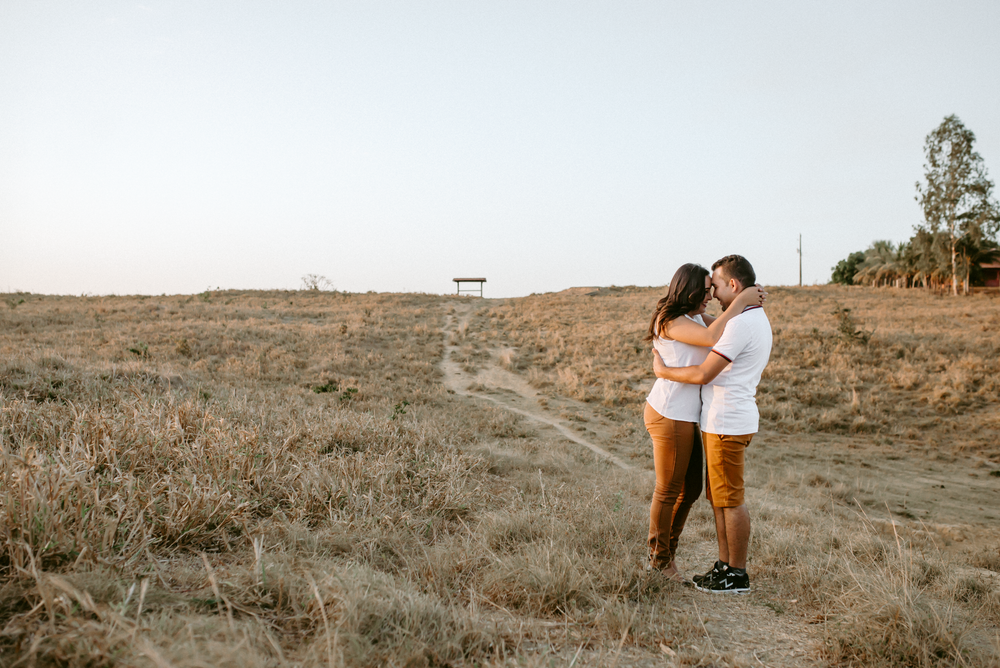 A couple lovingly embrace in a wide open field during sunset, symbolizing affection and connection.