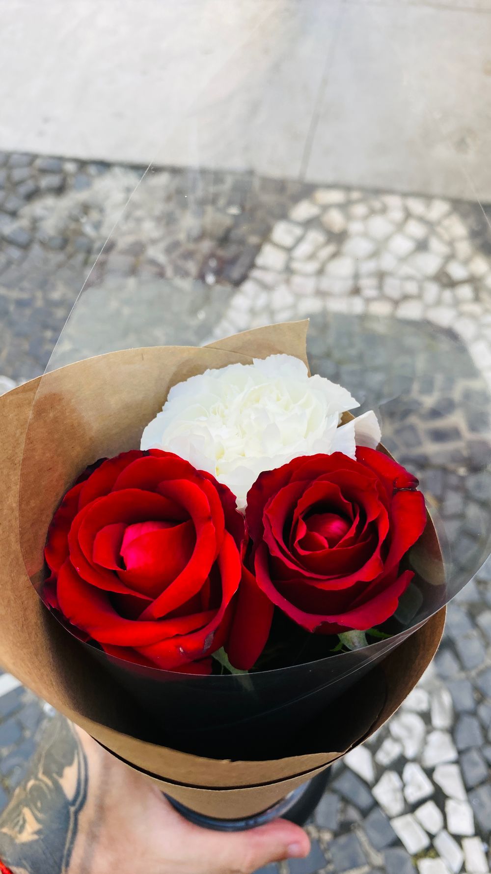 Close-up of a hand holding a bouquet of red and white roses on a cobblestone street.
