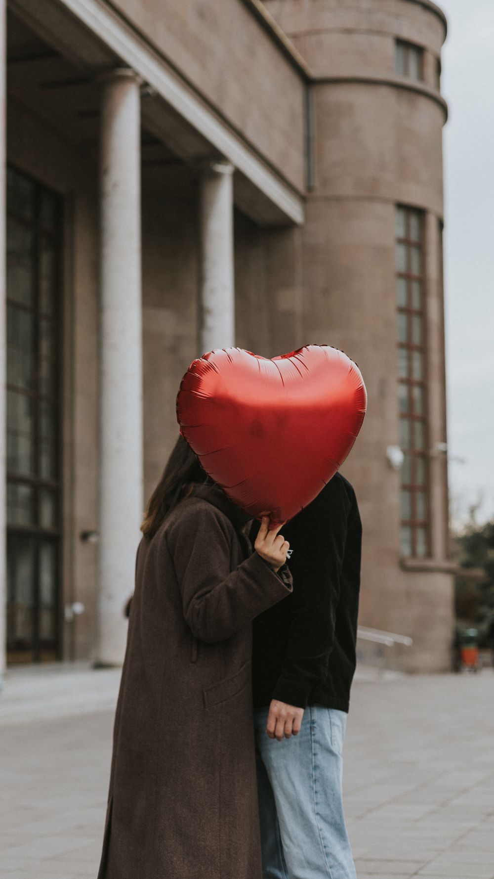 A couple embraces with a heart-shaped balloon in an urban setting, expressing love.