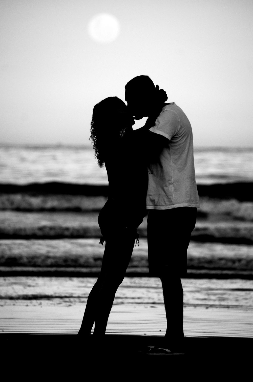 Silhouette of a couple kissing on the beach at sunset, reflecting romance and tranquility.