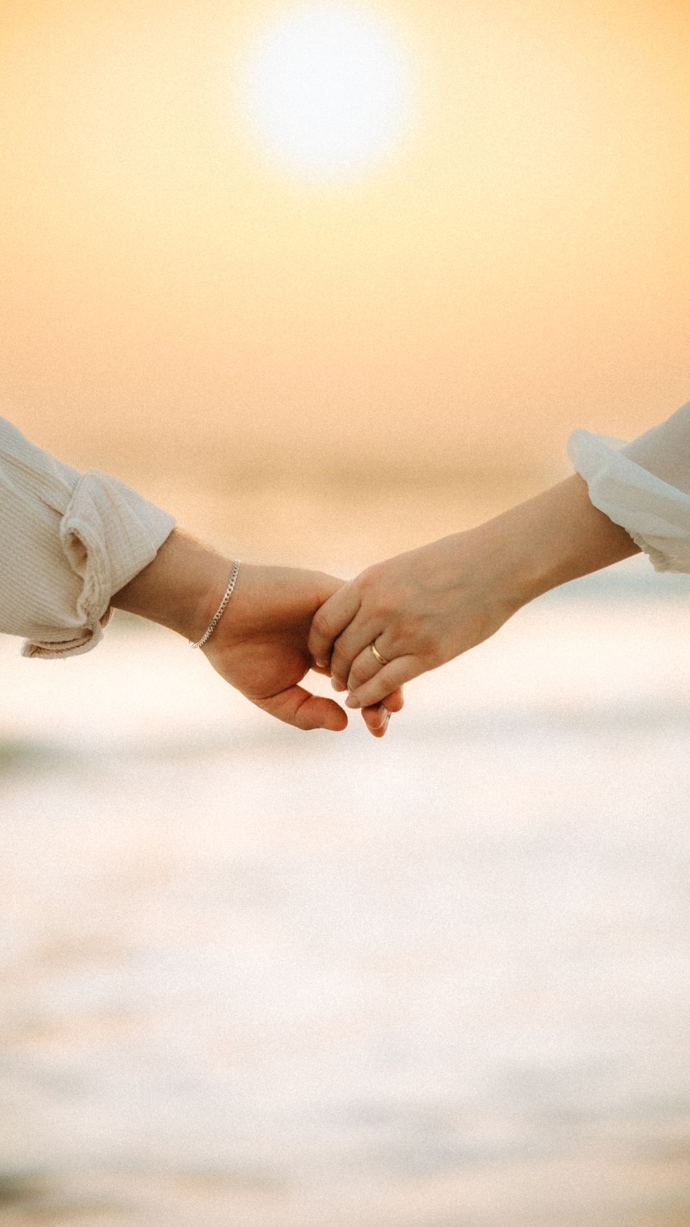 Close-up of couple's hands holding at sunset by the sea, symbolizing love and romance.