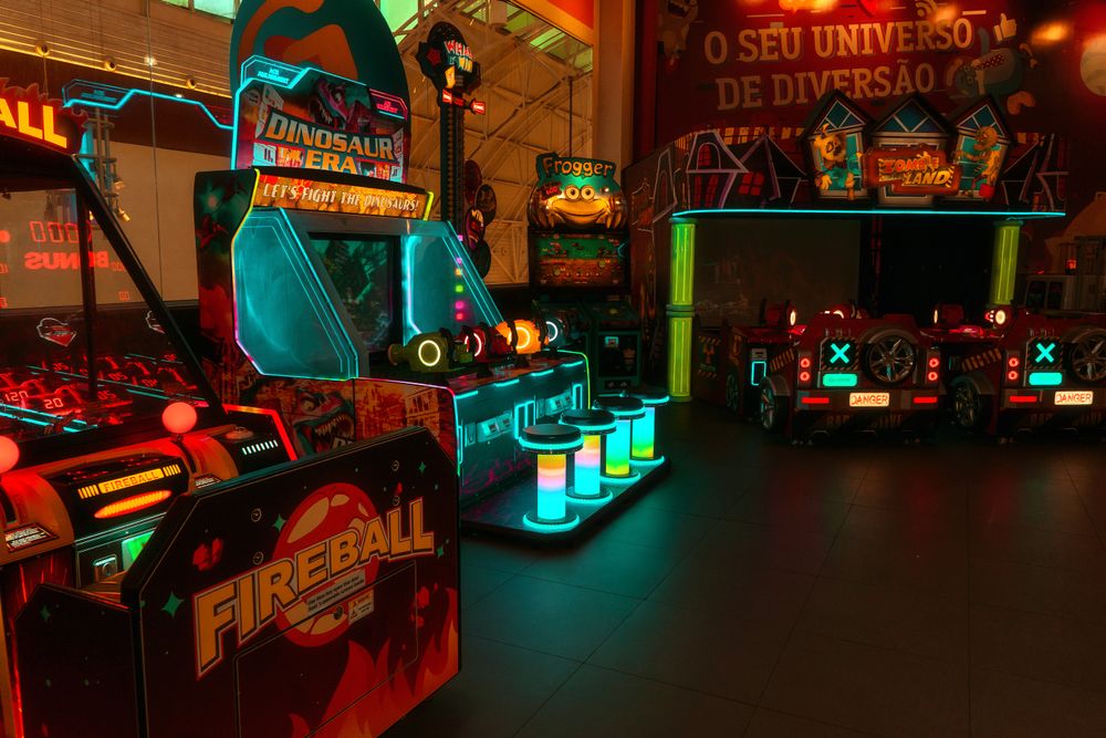 Kleurrijke neon-verlichte arcade met verschillende spelmachines waaronder fireball en dinosaurus tijdperk.