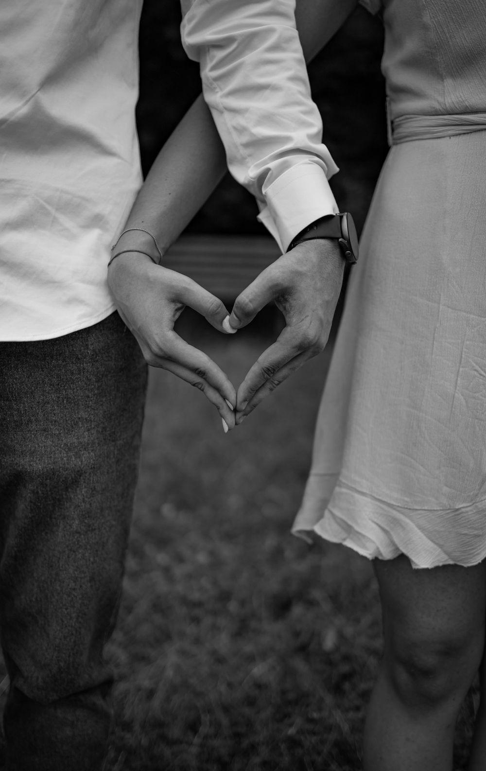 Black and white photo of couple forming a heart with their hands, symbolizing love.