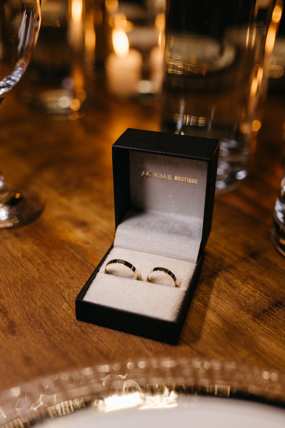 Luxurious wedding rings in a boutique box on a wooden table with romantic candlelight.
