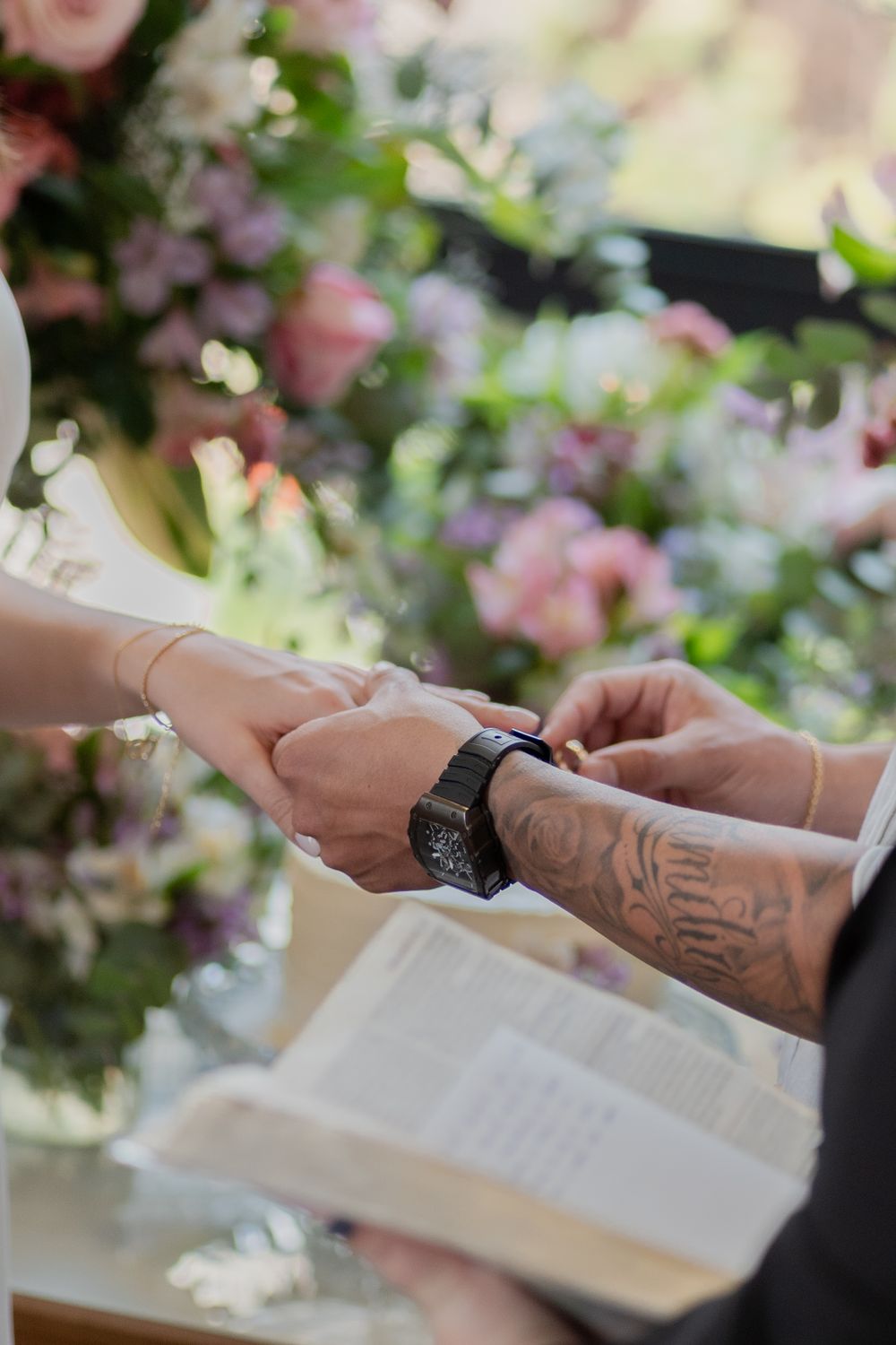 Close-up of a couple exchanging rings at an indoor wedding, surrounded by beautiful floral arrangements.