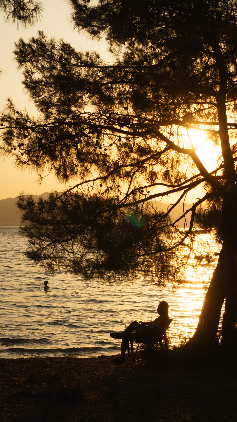 A tranquil lakeside scene depicting a silhouette of a person relaxing by the shore during sunset.