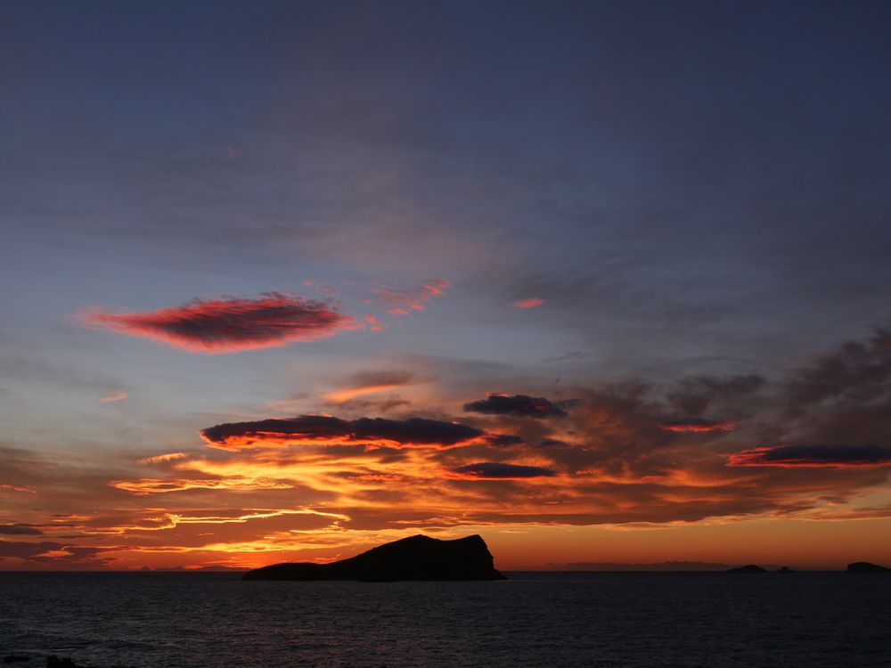 Stunning sunset over Cala Comte, Ibiza with dramatic clouds and vibrant colors.