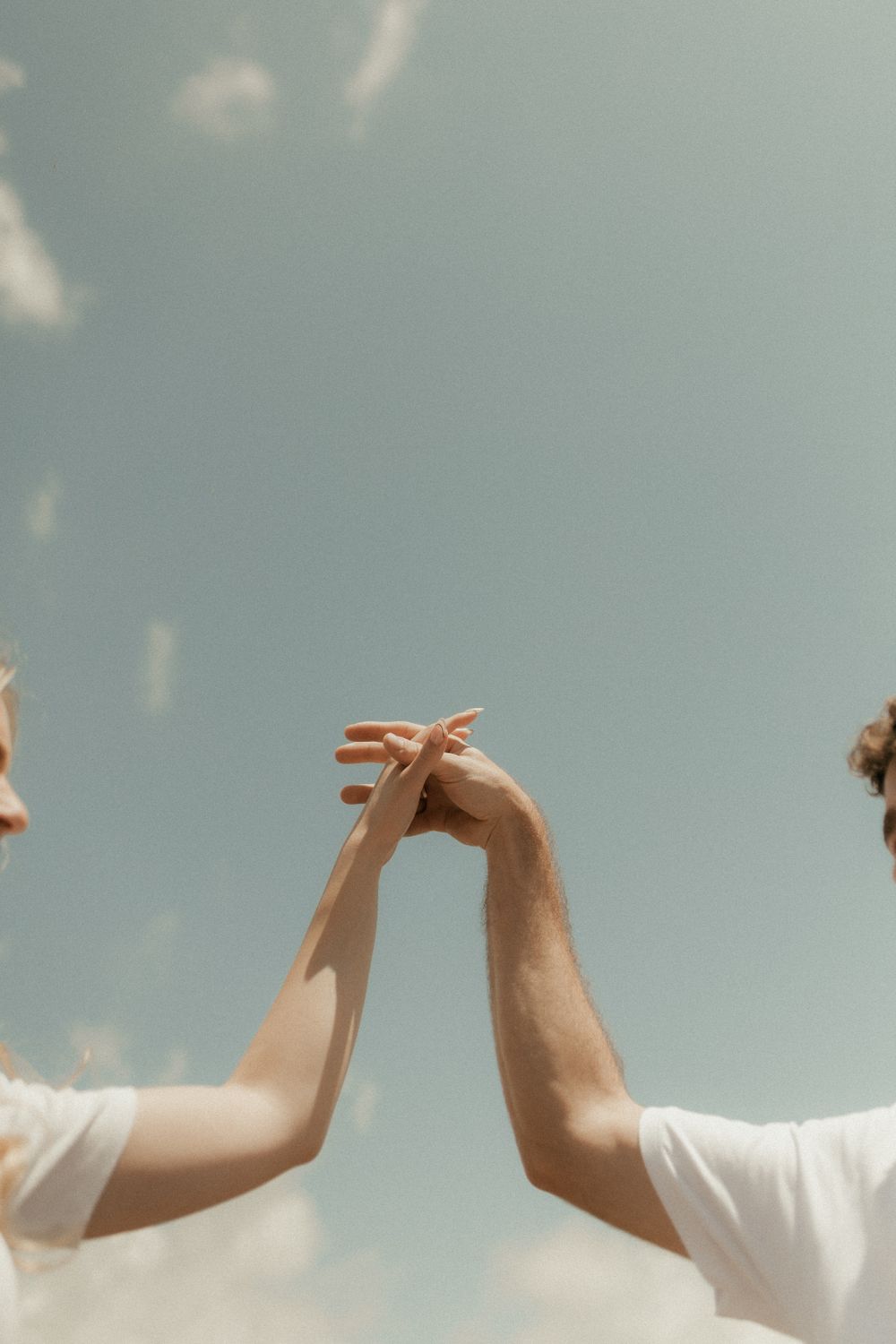Close-up of a couple holding hands against a blue sky, symbolizing unity and love.