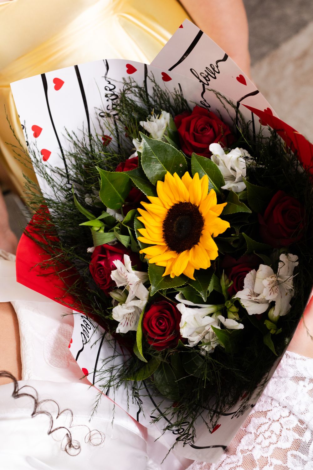 Elegant wedding bouquet featuring a bright sunflower with red roses and white lilies, perfect for a romantic celebration.