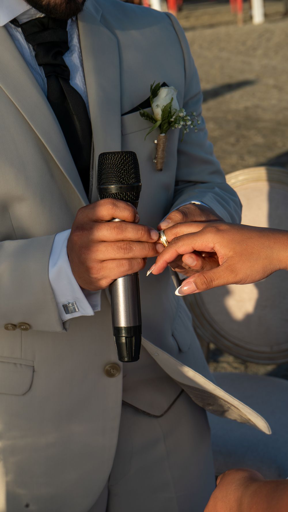 Close-up of a groom placing a ring on the bride's finger during an outdoor wedding ceremony.