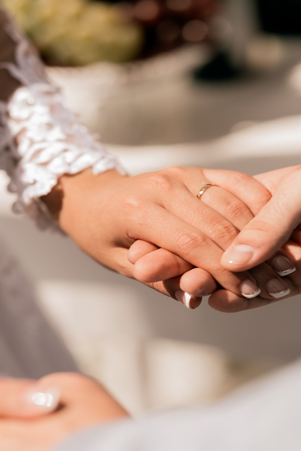 Intimate close-up of bride and groom holding hands, showcasing wedding rings during a ceremony.