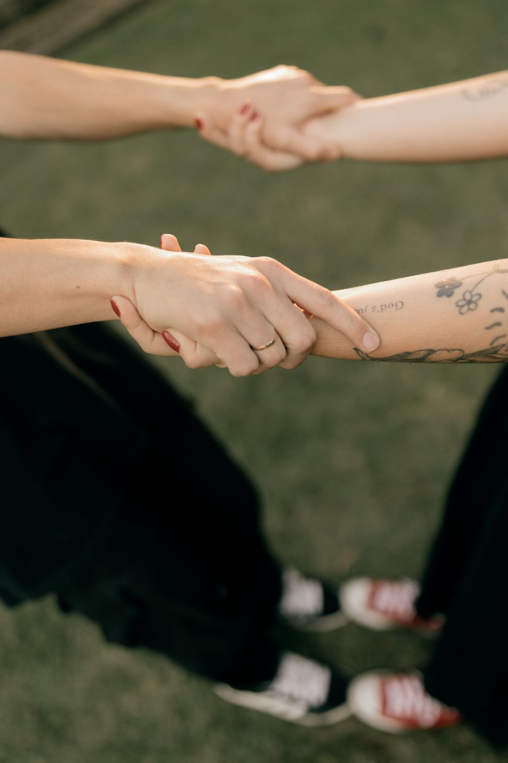 Close-up of two people holding hands, showcasing tattoos and casual style.