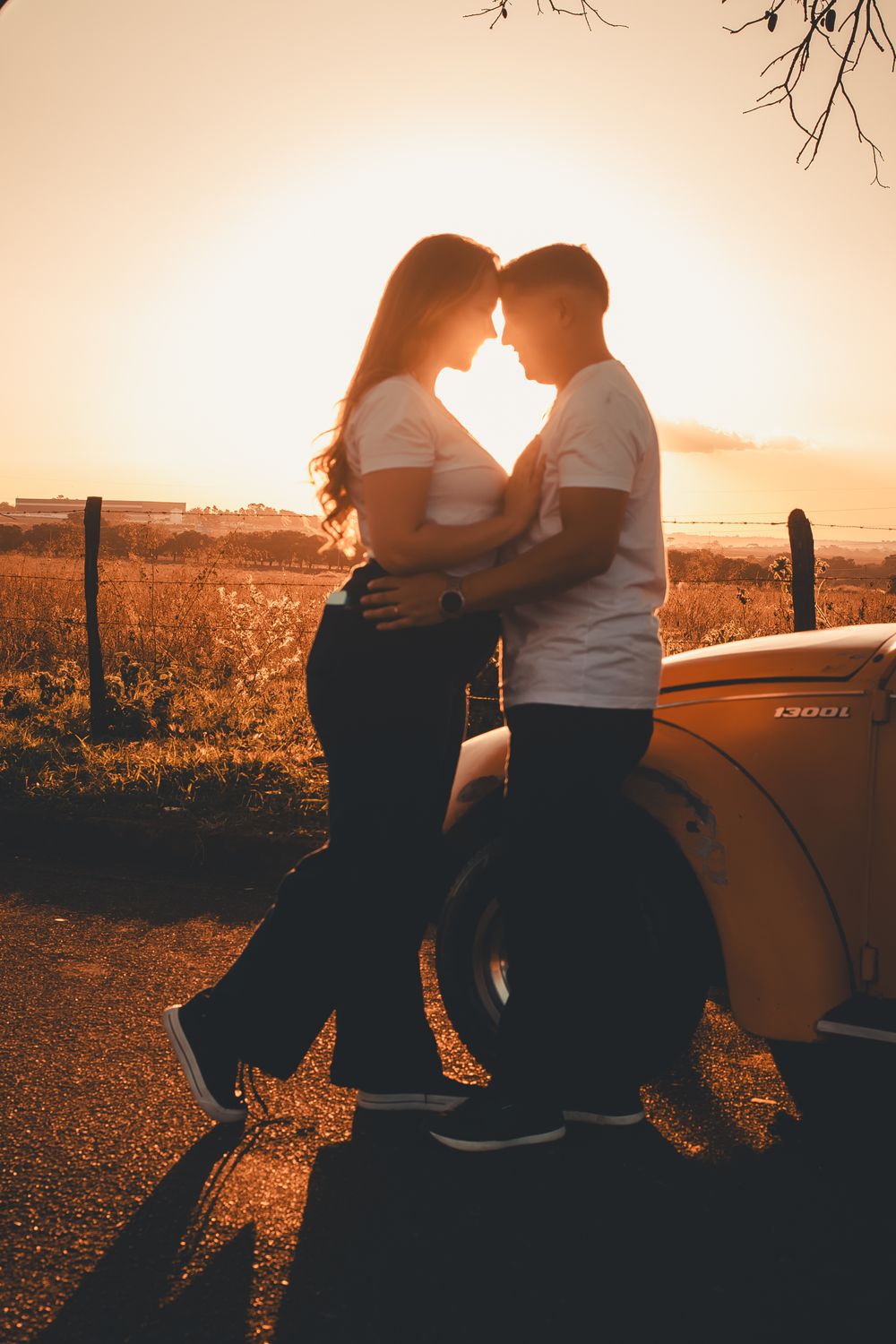 A couple embraces near a vintage car at sunset, highlighting romance and warmth.