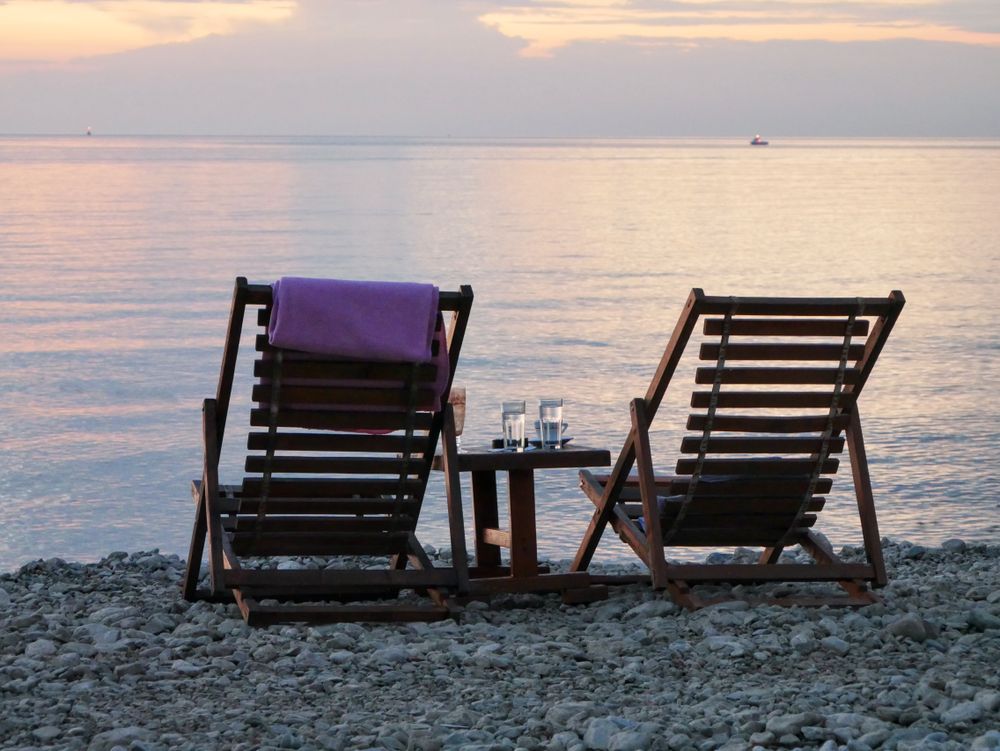 Dvě lehčí židle s nápoji na skalnaté pláži při západu slunce, Perfektní pro relaxaci.