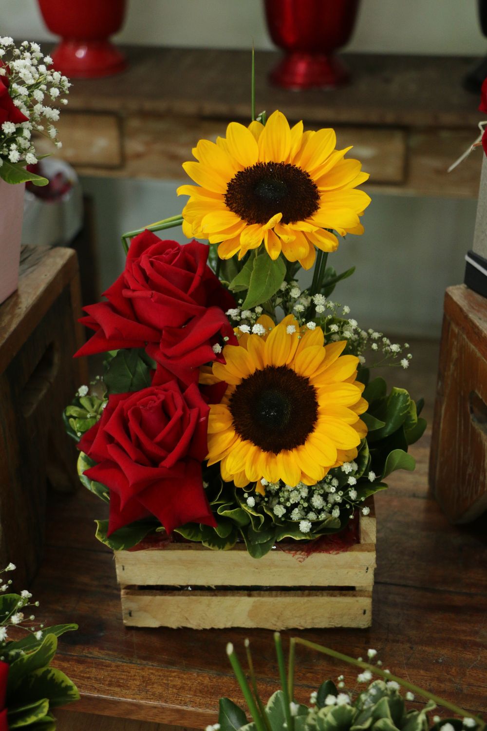 Stunning vertical flower arrangement featuring sunflowers, red roses, and greenery in a wooden box.