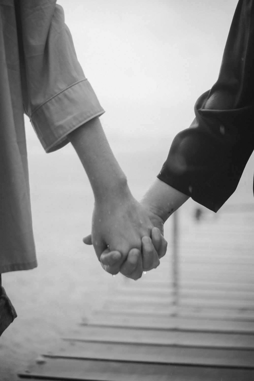 Artistic black and white photo of two people holding hands on a rainy day.